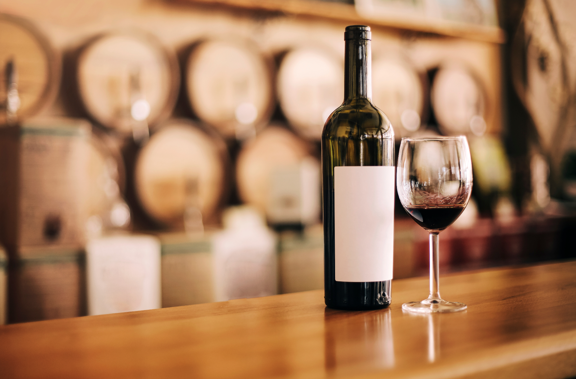 Bottle of Bulgarian red wine and a poured glass on a wooden bar in front of oak ageing barrels